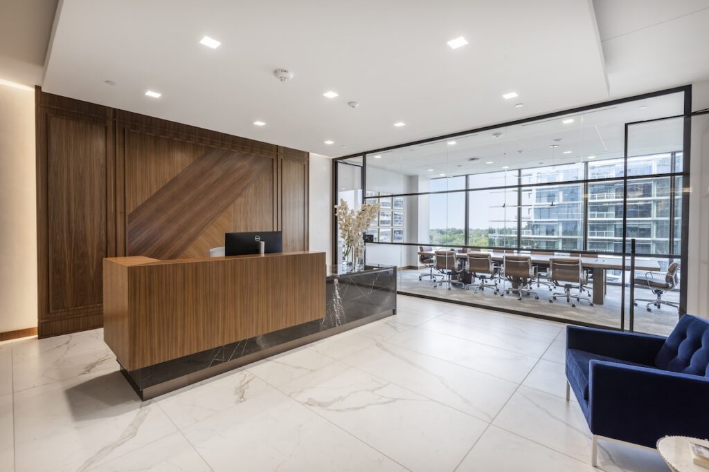 modern lobby of a car dealership - a desk with a wood paneled wall behind it and a glass wall looking into a board room